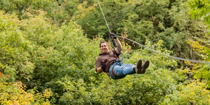 Ausflug mit Kindern - Rheinland-Pfalz - Ziplining bei EifelAdventures bedeutet, dass du entlang gespannter Stahlseile von Baum zu Baum gleitest, während du fest mit einem Gurtsystem verbunden bist. Die Zipline-Tour bei EifelAdventures ist nicht auf eine einzige Bahn begrenzt, sondern führt dich in Begleitung von professionell ausgebildeten Tour-Guides ca. 2,5 Stunden durch einen wundervollen Vulkaneifel-Wald. - Freizeitpark EifelAdventures